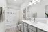 Bathroom with quartz counters, large mirror, vanity lighting, and white cabinetry