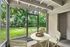 Charming porch area with elegant white table set, surrounded by lush greenery, blending indoor and outdoor living seamlessly.