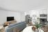 Bright and modern apartment living space featuring an open-concept kitchen with sleek stainless steel appliances, a cozy seating area with a stylish couch facing a large flat-screen TV, and a charming dining set with a centerpiece of fresh fruit.
