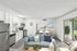 Bright and inviting living space featuring a modern kitchen with stainless steel appliances, cozy dining area, and comfortable seating, opening to a lush patio view.