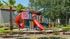 Charming apartment complex playground with vibrant slides, surrounded by lush greenery and palm trees, perfect for playful afternoons.