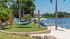 Serene lakeside retreat featuring relaxing hammocks, lush greenery, and inviting blue lounge chairs under umbrellas.