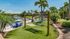 Lakeside oasis with inviting hammocks, vibrant blue Adirondack chairs, and lush tropical landscaping under a clear blue sky.