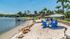 Tranquil lakeside retreat featuring a sandy beach, vibrant blue chairs, and lush palm trees, perfect for relaxation and leisure.