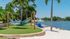Serene lakeside setting with cozy blue hammocks and Adirondack chairs on sandy shores, surrounded by lush palm trees.
