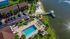 Breathtaking aerial view of a modern riverside apartment complex with a sparkling pool, lush green landscapes, and a scenic boardwalk.