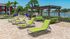 Luxurious poolside retreat with vibrant green lounge chairs, cozy outdoor seating under a stylish pergola, surrounded by lush palm trees and tranquil water views.
