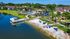 Scenic apartment complex with a tranquil lakeside view, featuring landscaped greenery, inviting pool area, and vibrant beach chairs under palm trees.