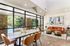 Clubhouse with modern furniture, featuring a striking orange sofa and artistic decor. Large windows offer a breathtaking view of a lush green landscape and pool.