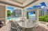Outdoor kitchen with sleek countertops overlooking a swimming pool, framed by lush greenery and stylish apartment buildings, perfect for entertaining.