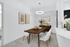 Elegant dining area featuring a sleek wooden table, plush white chairs, and modern artwork, with a stylish circular light fixture enhancing the space.
