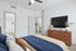 Elegant bedroom with a cozy bed, stylish dresser, and a wall-mounted TV, featuring a modern ensuite bathroom and a glimpse of the dining area.