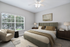 Elegant bedroom with plush bedding, stylish armchair, and natural light streaming through large windows.
