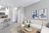 Modern open-concept living space with stylish d&eacute;cor, cozy beige sofa, vibrant artwork, and sleek kitchen with breakfast bar seating.