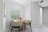 Bright dining nook with a round wooden table set for four, offering a cozy ambiance with natural light from a large window overlooking greenery.