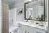 Elegant bathroom featuring a sleek countertop, large mirror, modern fixtures, and a cozy shower area with stylish decor.