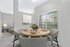 Bright and inviting dining area with a stylish wooden table set against large windows, offering an elegant view of the lush greenery outside.