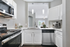 Modern kitchen with sleek stainless steel appliances, elegant white cabinetry, and under-cabinet lighting, opening into a bright living area.