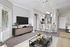 Bright and inviting living space with a cozy atmosphere, featuring modern furniture, a wall-mounted TV, and a sleek kitchen with a breakfast bar.
