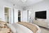 Contemporary bedroom featuring a cozy bed, wall-mounted TV, ensuite bathroom, and walk-in closet, bathed in natural light.
