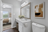 Elegant modern bathroom with sleek vanity, large mirror, stylish artwork, and a glimpse into a cozy, well-lit bedroom.