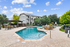Luxurious apartment community with a sparkling pool, inviting seating area, and lush greenery under a vibrant blue sky.