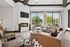 Inviting modern clubhouse with large windows, stylish fireplace, and comfortable seating, offering a lush garden view.
