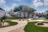 Charming apartment community with well-manicured green spaces, shaded seating areas, and picturesque walking paths under a vibrant blue sky.