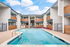 Inviting apartment community with a sparkling pool, modern wood accents, and serene outdoor lounging area under a bright blue sky.