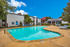 Inviting apartment pool area with crystal-clear water, surrounded by comfortable lounge chairs and lush landscaping under a bright blue sky.