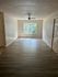 Bright and spacious living area in an unfurnished apartment, featuring sleek wooden flooring and a large sunlit window.