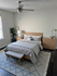 Serene bedroom featuring a plush bed with elegant gray bedding, surrounded by tasteful wood furniture and vibrant green plants under a stylish ceiling fan.
