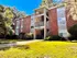 Charming brick apartment building with a spacious grassy front yard and lush greenery, basking in bright sunlight.