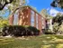 Charming red-brick apartment building surrounded by lush greenery and clear blue skies.