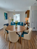 Chic dining and living space with a round wooden table, stylish chairs, and a comfortable blue sofa. Bright natural light enhances the elegant decor and modern finishes.