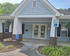 Charming blue and white facade of a home with inviting porch and wheelchair-accessible parking spot, surrounded by lush greenery.