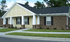Charming single-story duplex with brick facade and inviting front porch, nestled in a serene neighborhood with lush greenery.