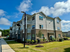Modern apartment complex with pristine landscaping under a bright blue sky, featuring balconies and large windows for natural light.