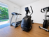 Bright home gym with modern exercise equipment and large windows overlooking a lush garden.