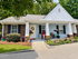 Charming single-story home with a welcoming front porch adorned with colorful potted plants, set amidst lush greenery.