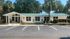 Charming white brick building with green metal roof, surrounded by lush landscaping and palm trees, ample parking in front.