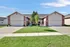 Charming duplex with brick facade and two-car garage, nestled in a serene suburban setting with lush green lawn.