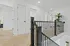 Bright and modern hallway with elegant wooden railing, plush carpet, and stylish recessed lighting, leading to multiple inviting rooms.