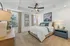 Elegant bedroom with a cozy queen-sized bed, stylish ceiling fan, and tasteful artwork. Natural light pours through large windows, complementing the serene color palette and contemporary furnishings.