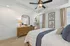 Inviting bedroom with stylish ceiling fan, elegant wood dresser, and cozy bed, bathed in natural light from large windows.