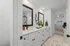Bright and elegant bathroom featuring dual sinks with sleek black fixtures, large mirrors, modern cabinetry, and a spacious walk-in closet.