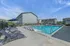 Inviting apartment community pool area with modern lounge chairs, sleek umbrellas, and pristine buildings under a bright blue sky.