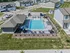 Inviting aerial view of modern apartment complex featuring a sparkling swimming pool with lounge chairs, surrounded by well-manicured greenery and contemporary homes.