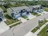 Charming suburban street view featuring modern townhouses, each with spacious driveways and well-maintained lawns, set against a lush green backdrop.