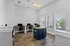 Bright and inviting home office space with four modern workstations, natural light streaming through large windows, and elegant wood flooring.